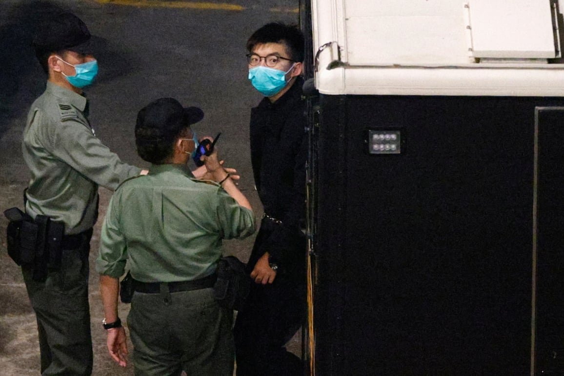 Two guards and a man in a dark blue suit, all wearing medical face masks